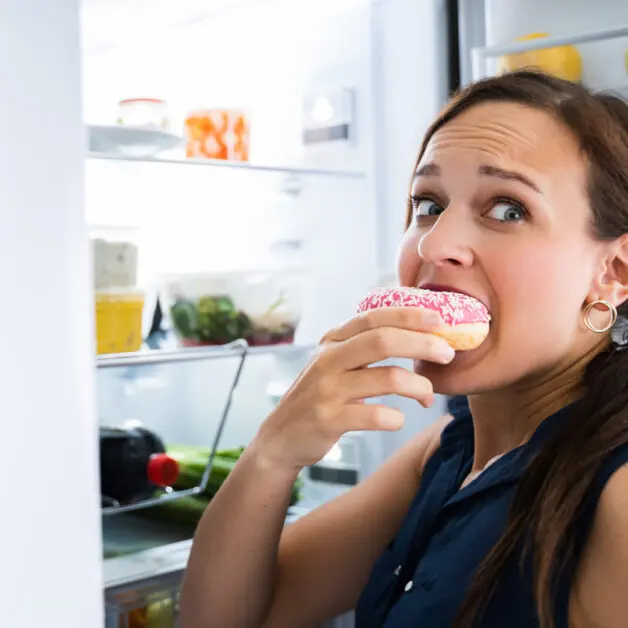 Overeating a donut in front of fridge and looking woried